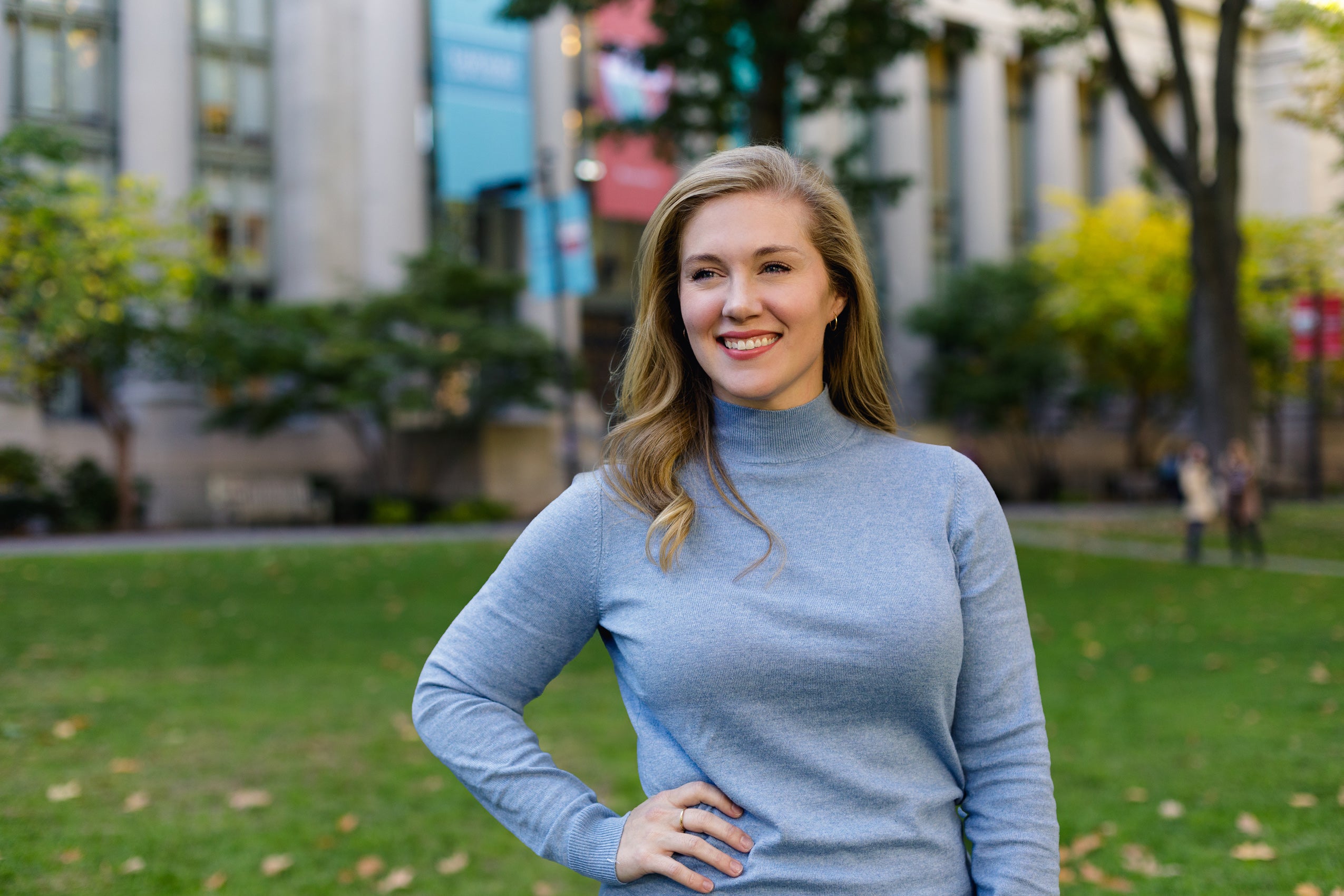 A woman in grey sweater poses in front of a building on the Harvard Law School campus.