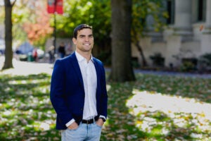 A man in a blue blazer poses in front of a building on the Harvard Law School campus.
