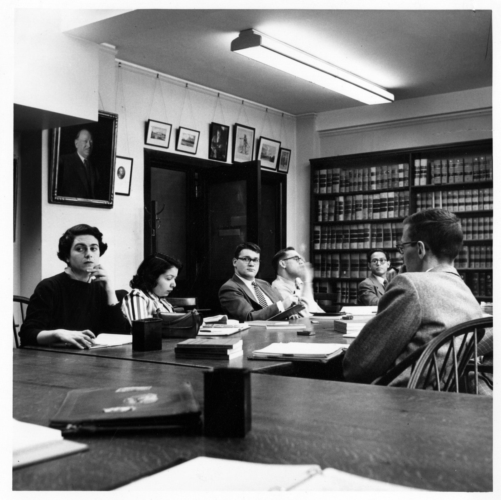 Two women sit at a long table with several men in a room lined with law books