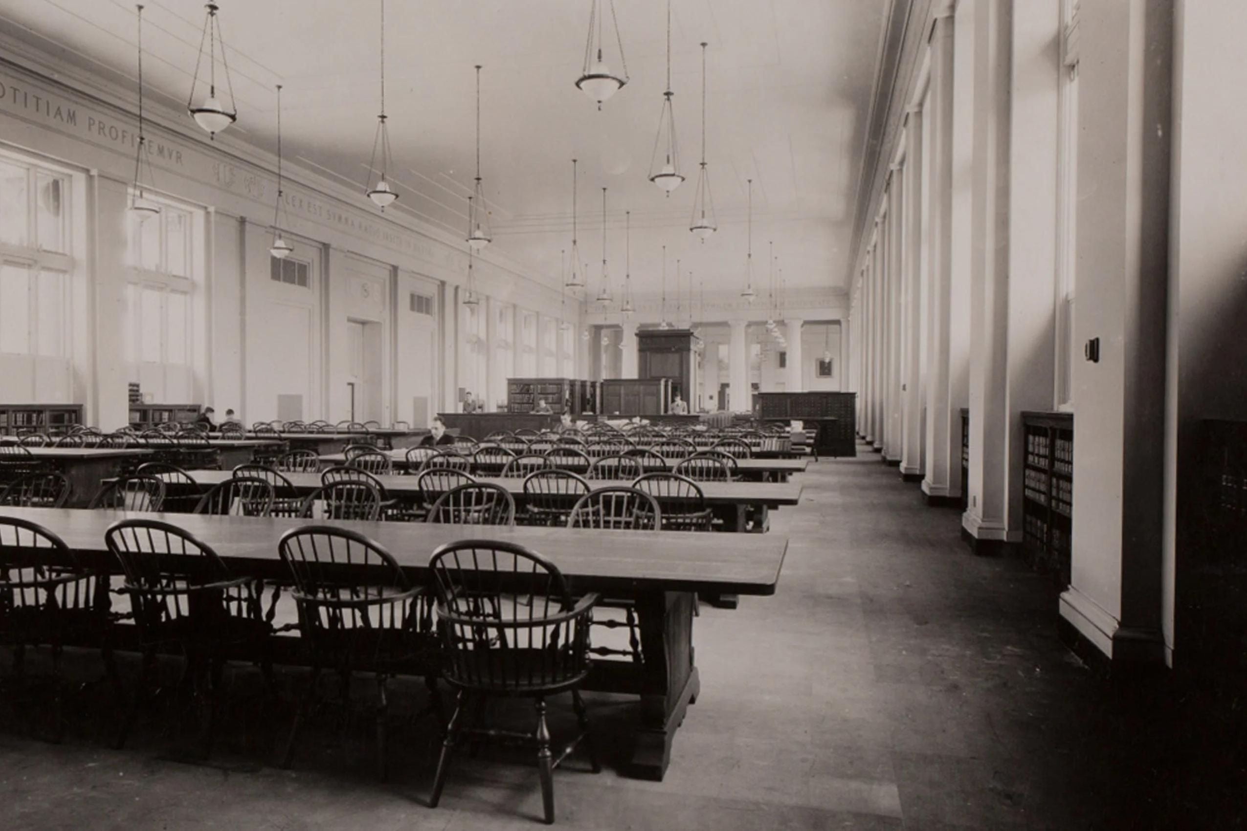 A black and white photo of a large room with wooden tables and chairs